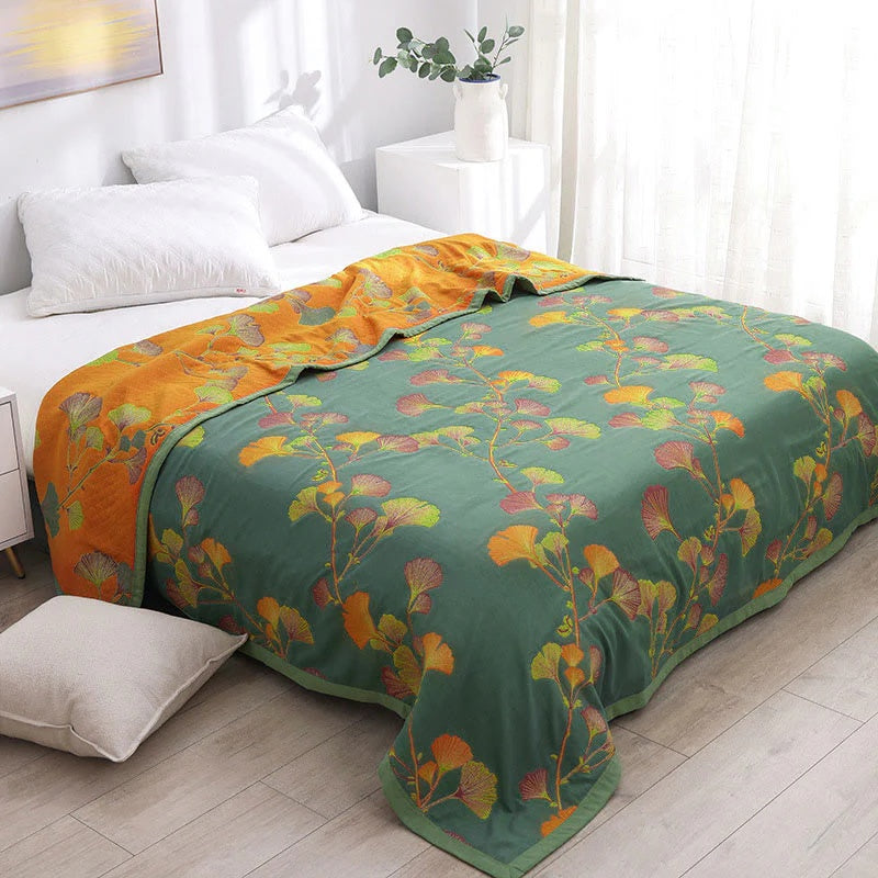 Green reversible coverlet with a floral ginkgo leaf pattern in orange and yellow on one side and orange floral ginkgo leaves on the other.