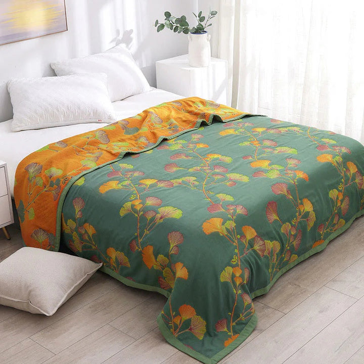 Green reversible coverlet with a floral ginkgo leaf pattern in orange and yellow on one side and orange floral ginkgo leaves on the other.