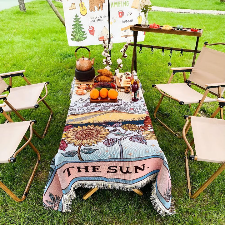 Boho style tapestry throw with a sun design, draped over a picnic table with chairs.