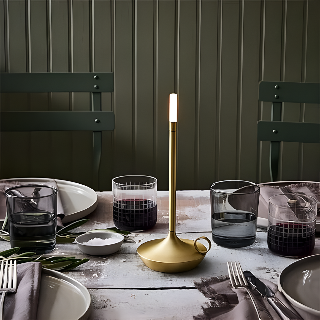 Portable aluminium table lamp with a warm glow on a dining table setting.