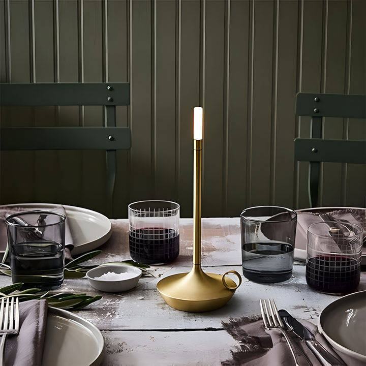 Portable aluminium table lamp with a warm glow on a dining table setting.