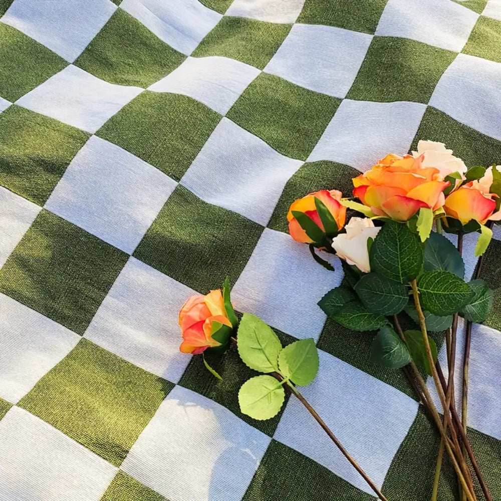 Fringed picnic blanket with green and white checkered pattern, with a bouquet of orange and white roses.