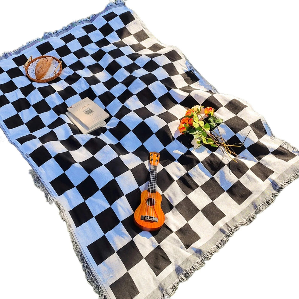 Black and white checkered picnic blanket with fringe, a ukulele, books, bread, and flowers.
