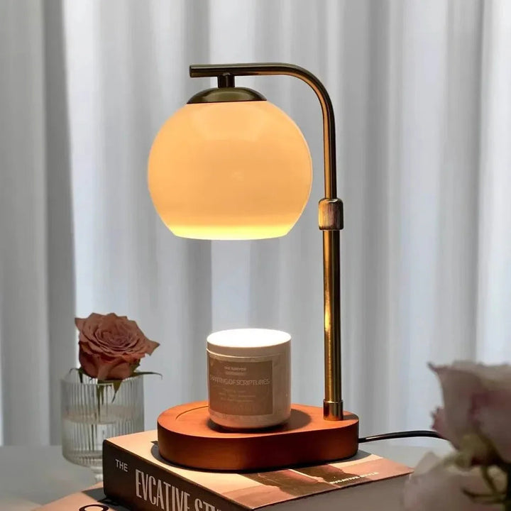 Sculpted glass candle warmer lamp with a retro amber glow, placed on a book next to a rose.