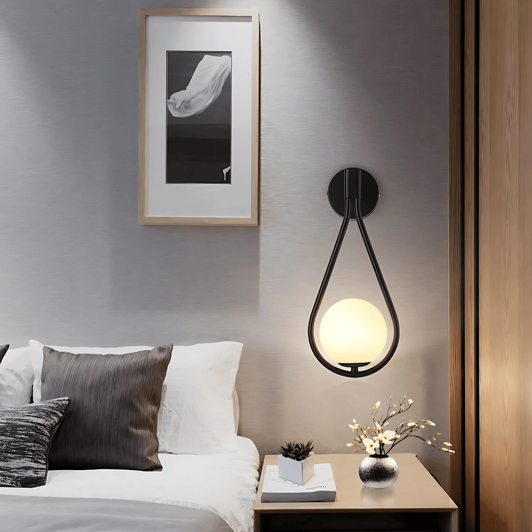 Black teardrop wall sconce with a frosted globe light above a bed.