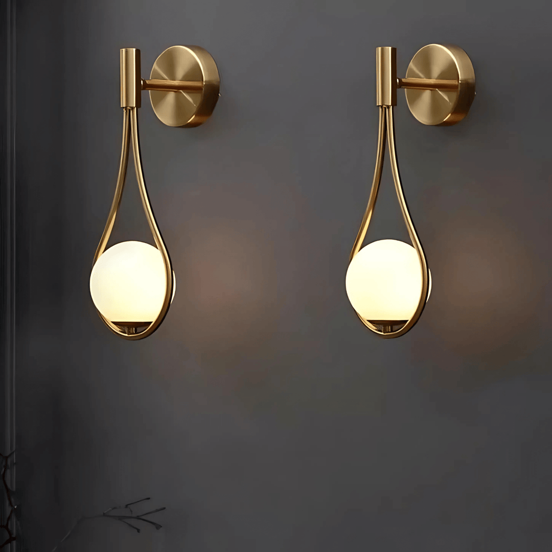 Two brass teardrop wall sconces with frosted glass globes mounted on a dark gray wall.