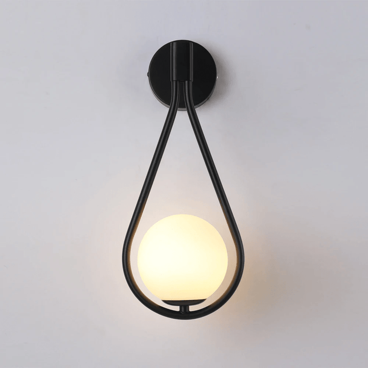 Black teardrop wall sconce with a frosted glass globe light against a white wall.