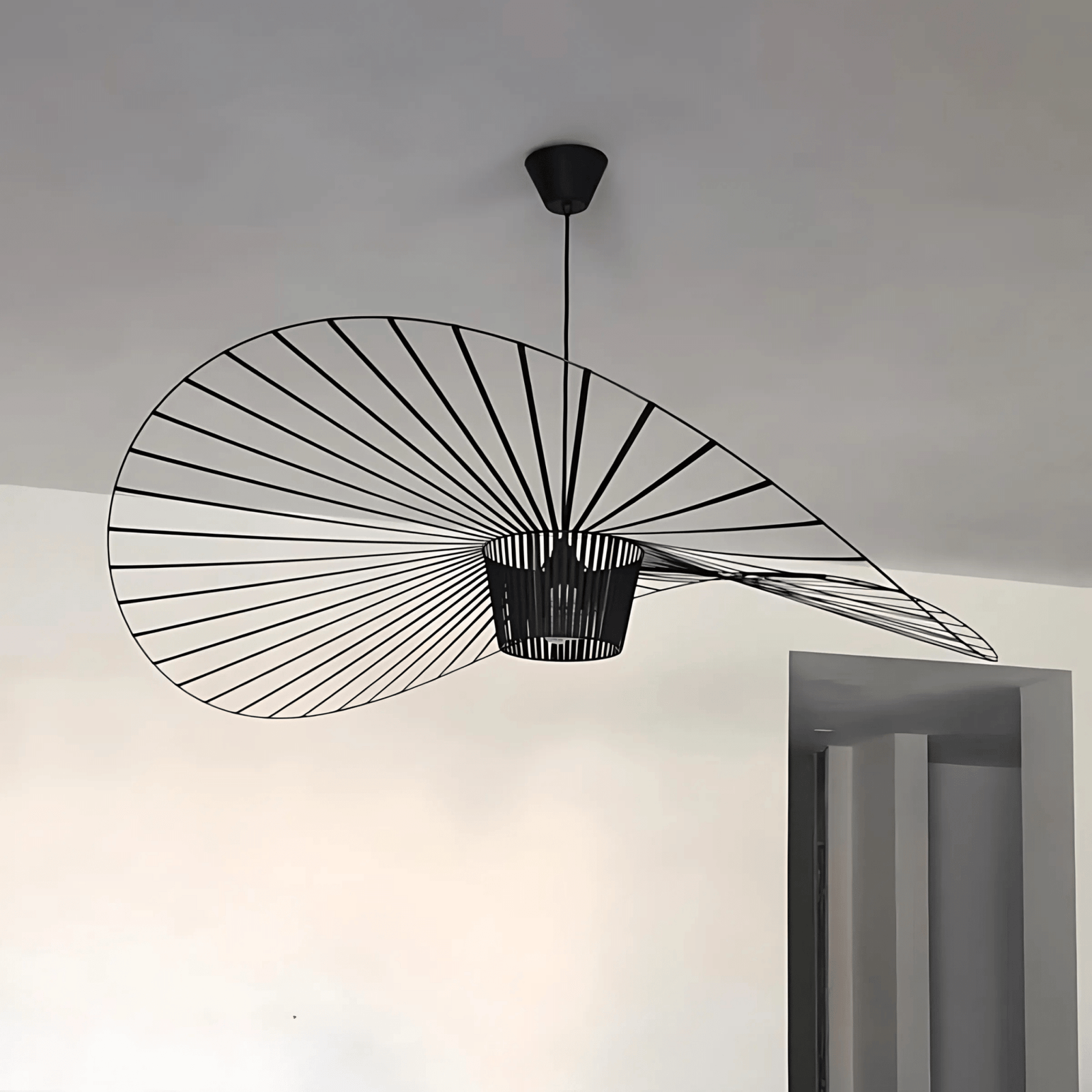 Black wire pendant light with a wide, flat shade resembling a hat, suspended from a black ceiling mount.