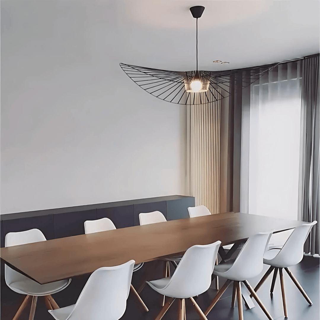 A modern dining room with a long wooden table and white chairs, illuminated by a unique black wire pendant light.