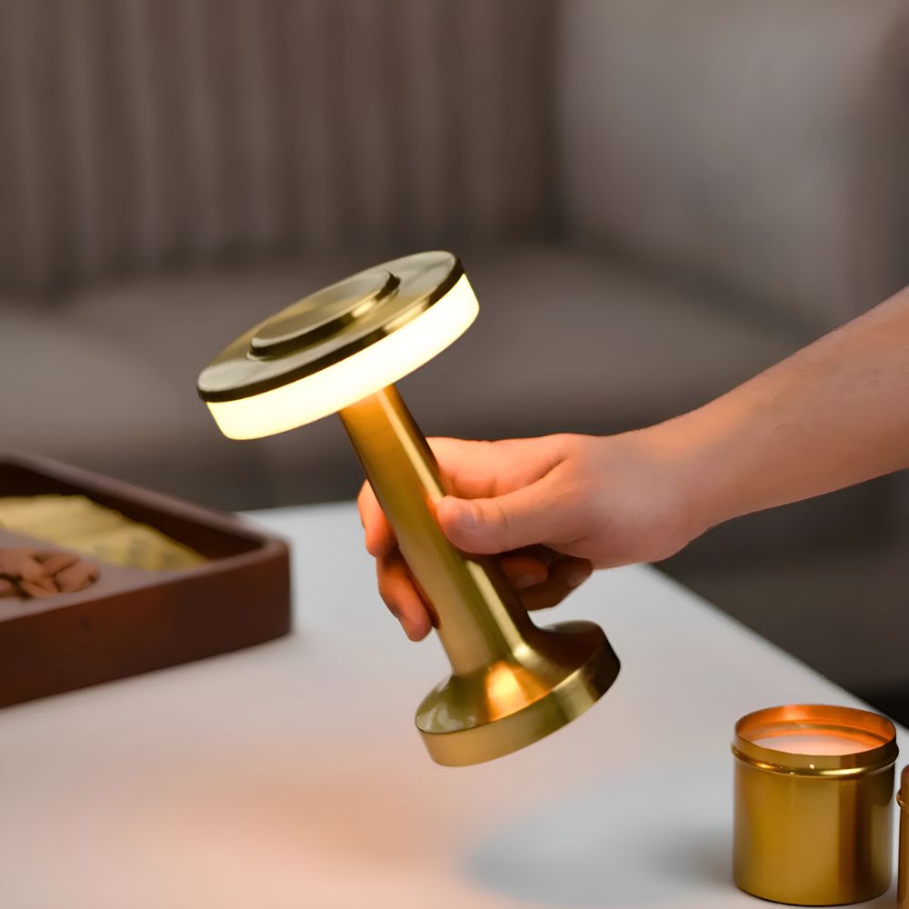 A hand holds a gold cordless table lamp with a warm ambient glow.