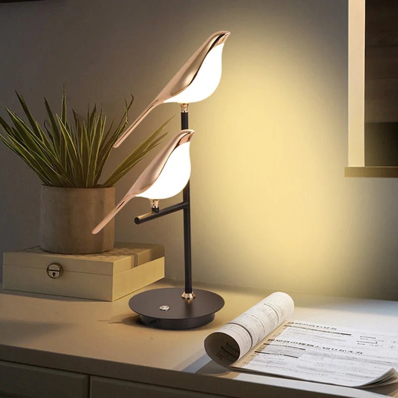 Two gold bird-shaped lamps with white frosted glass bodies on a black stand, casting a warm glow.