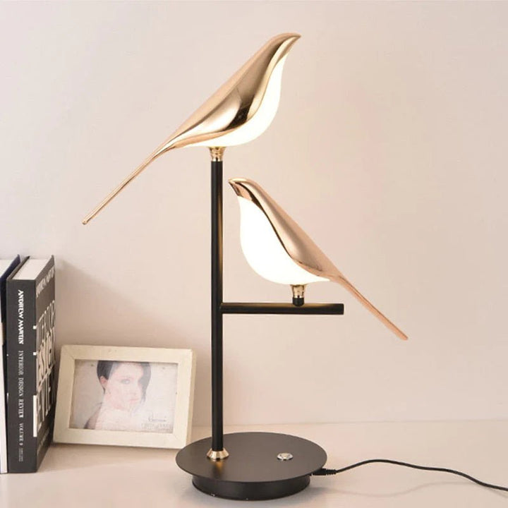Two gold bird-shaped lamps with white light, one above the other, on a black stand with a round base.