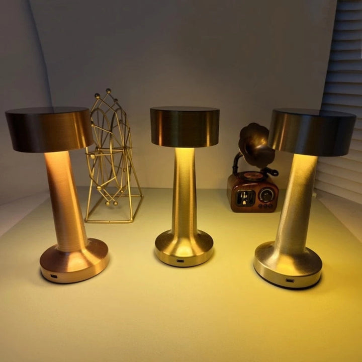 Three portable LED desk lamps in brushed gold and bronze finishes, with USB charging ports.