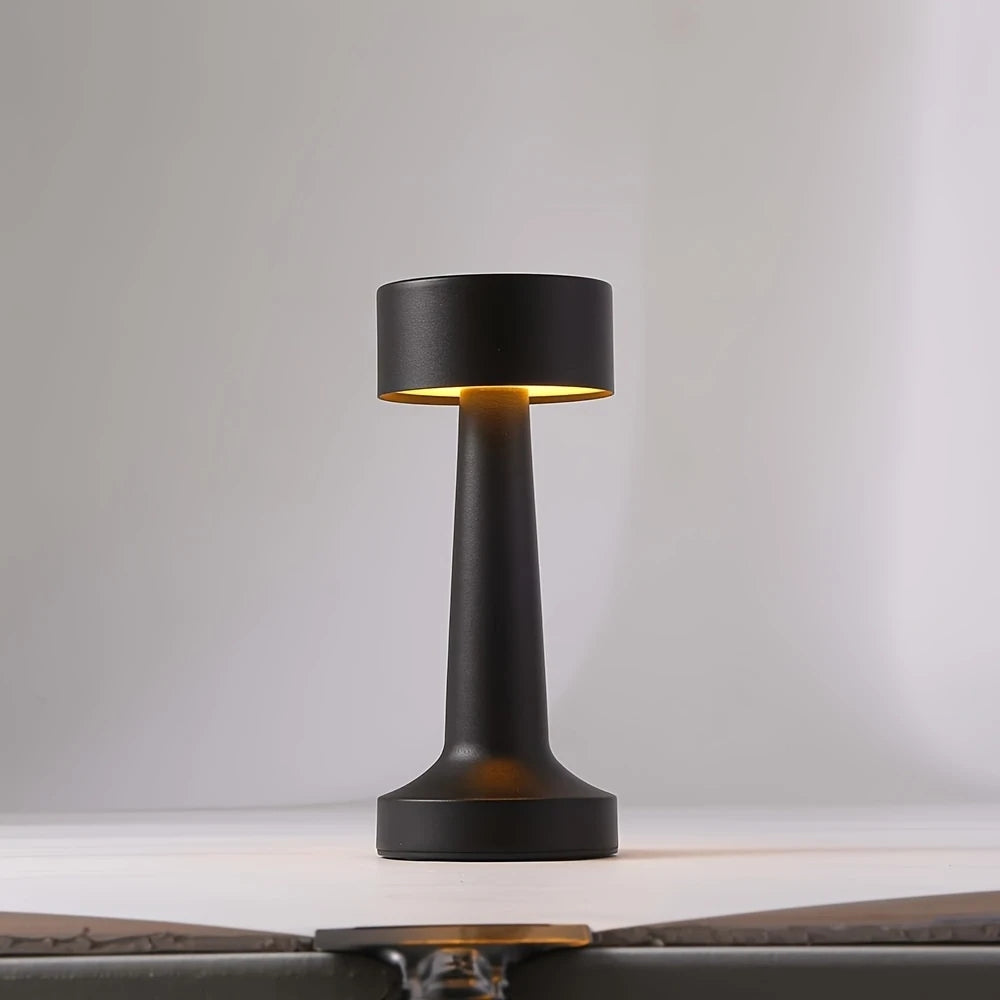 Black portable LED desk lamp with a cylindrical shade and a tapered base, emitting a warm light.
