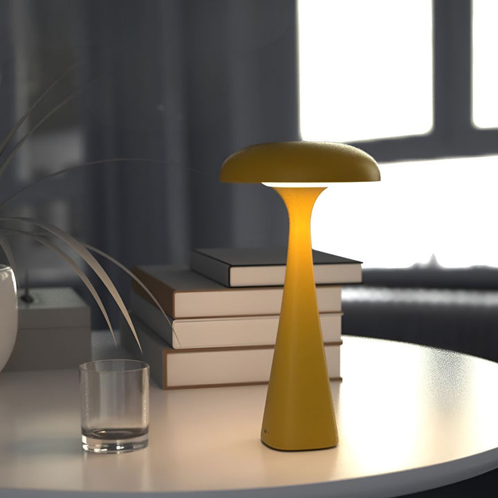 Yellow Jellyfish Desk Lamp with a soft ambient glow on a table with books and a glass.