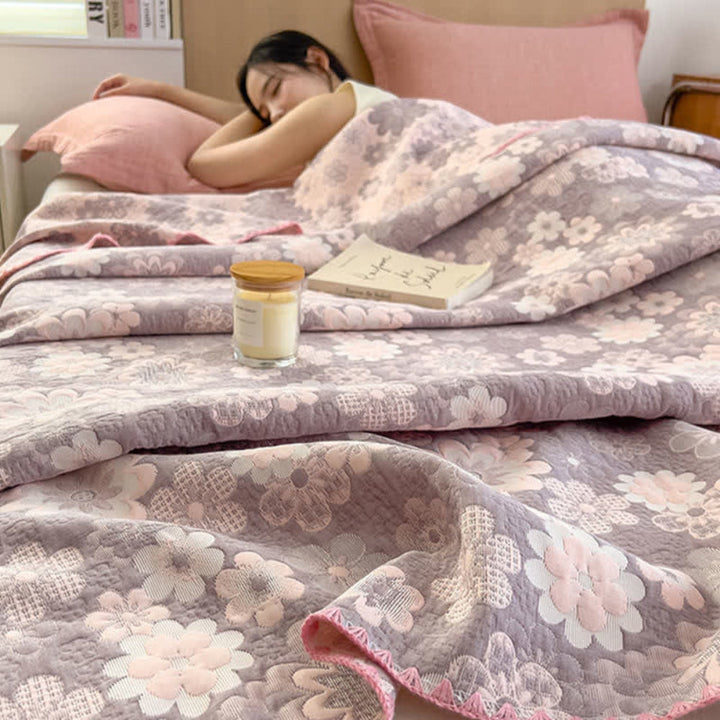 Reverie Floral Cotton Gauze Blanket draped on a bed with a woman sleeping.