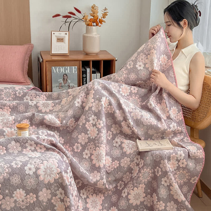 Woman sitting on a bed covered by a floral gauze blanket. The blanket has a pink and grey floral pattern.