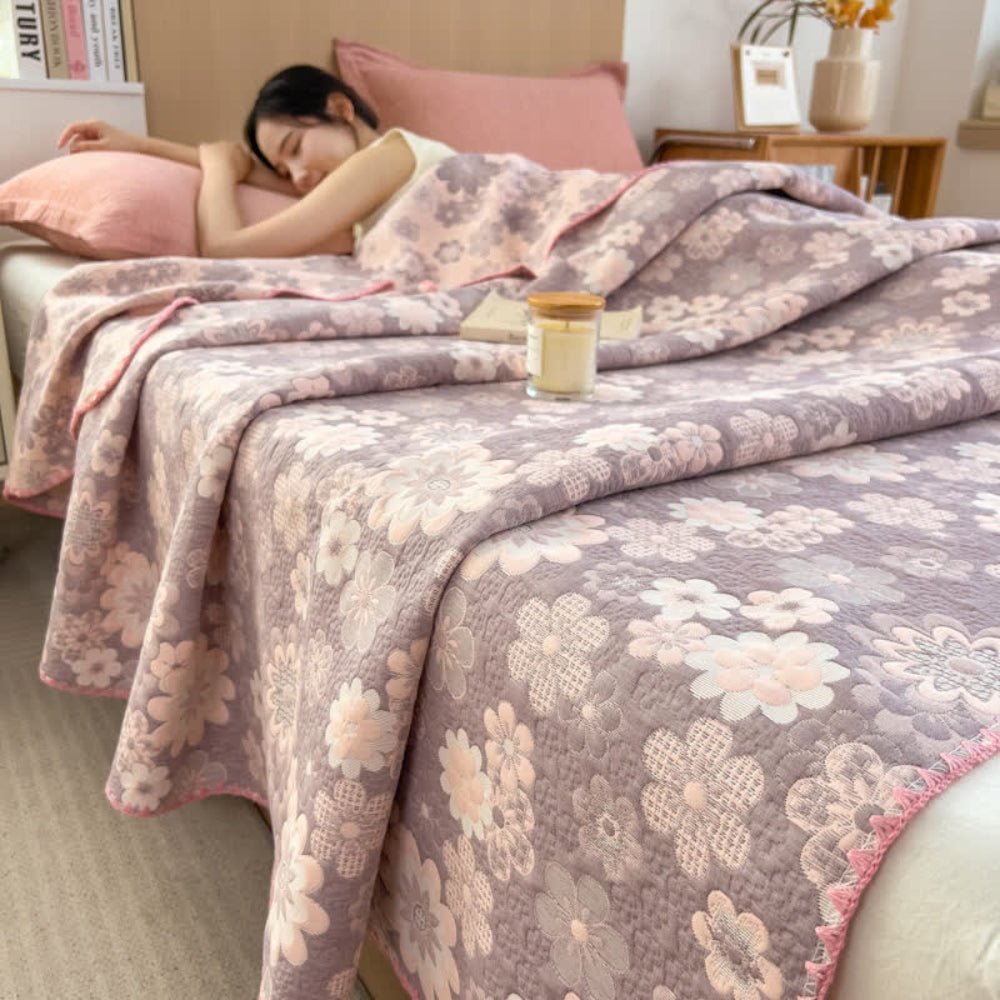 A woman sleeps under a floral cotton gauze blanket in shades of purple and pink.
