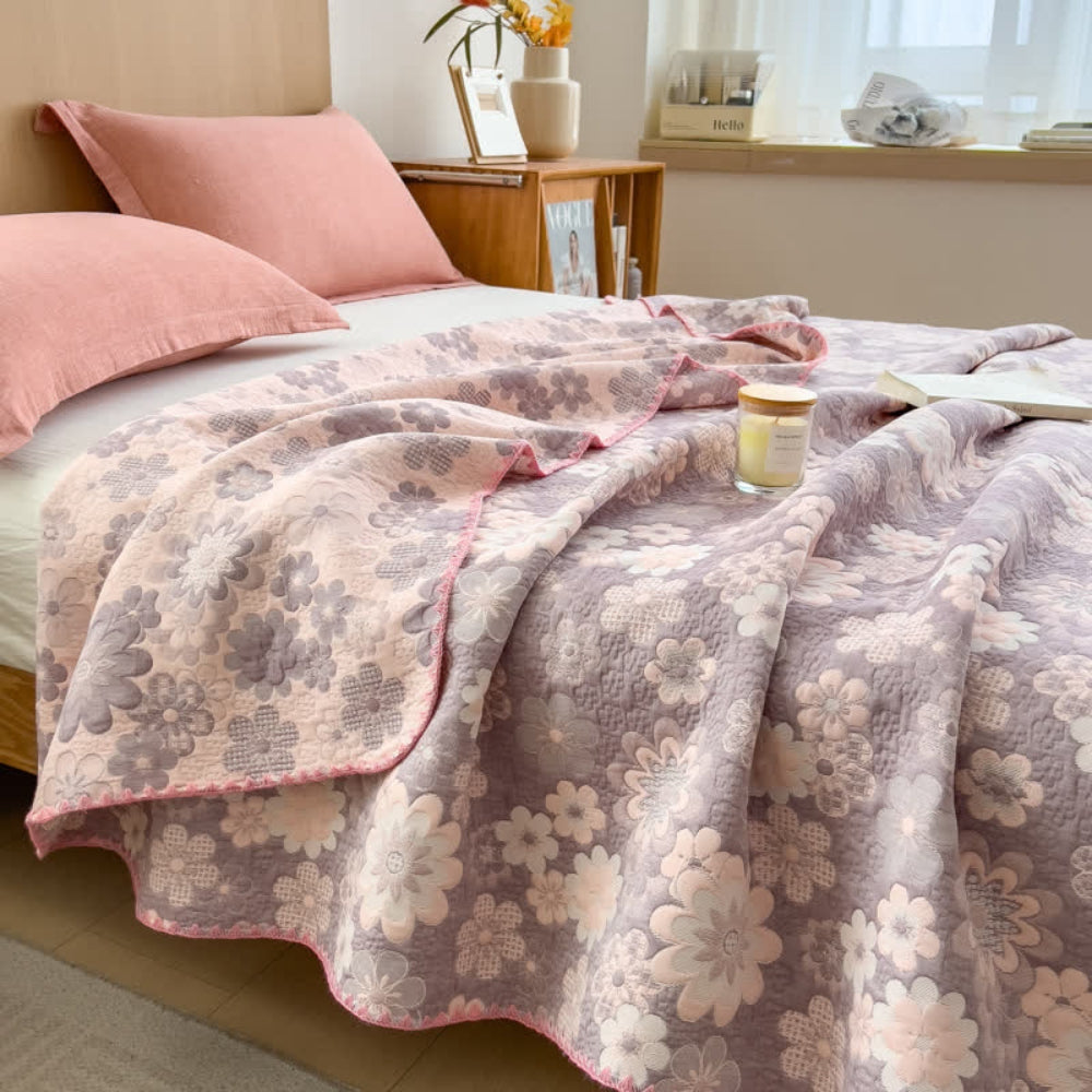 Reverie Floral Cotton Gauze Blanket in blush pink and grey floral pattern, draped on a bed with pink pillows.