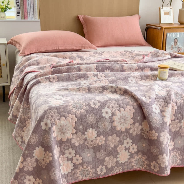 Reverie floral cotton gauze blanket in blush pink and grey on a bed with pink pillows.