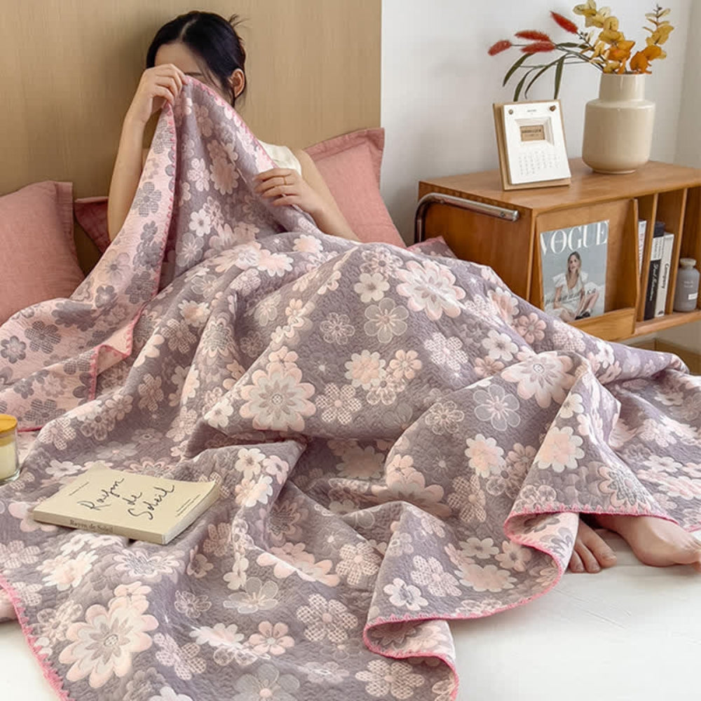 A woman is covered by a floral cotton gauze blanket with pink and gray flowers.