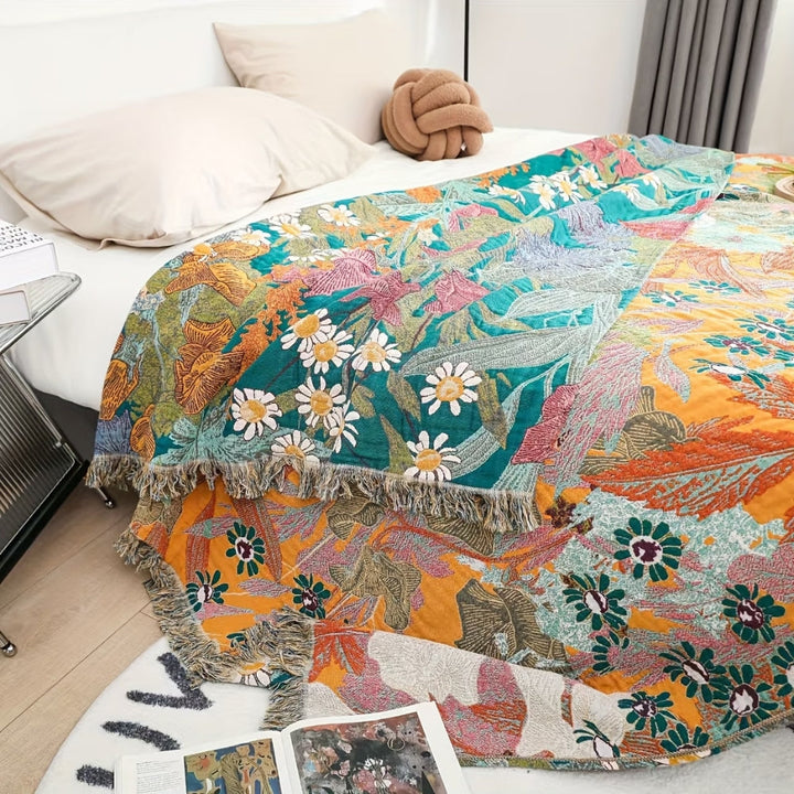 Bohemian floral patchwork tassel blanket with daisies and large leaves in teal, orange, and yellow.