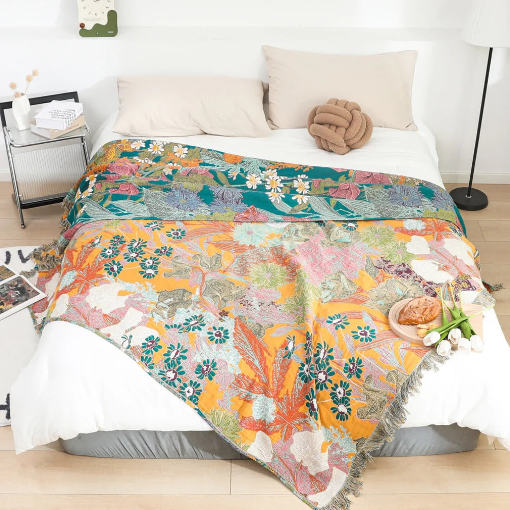 Bohemian floral patchwork tassel blanket in yellow, teal, and pink on a bed.