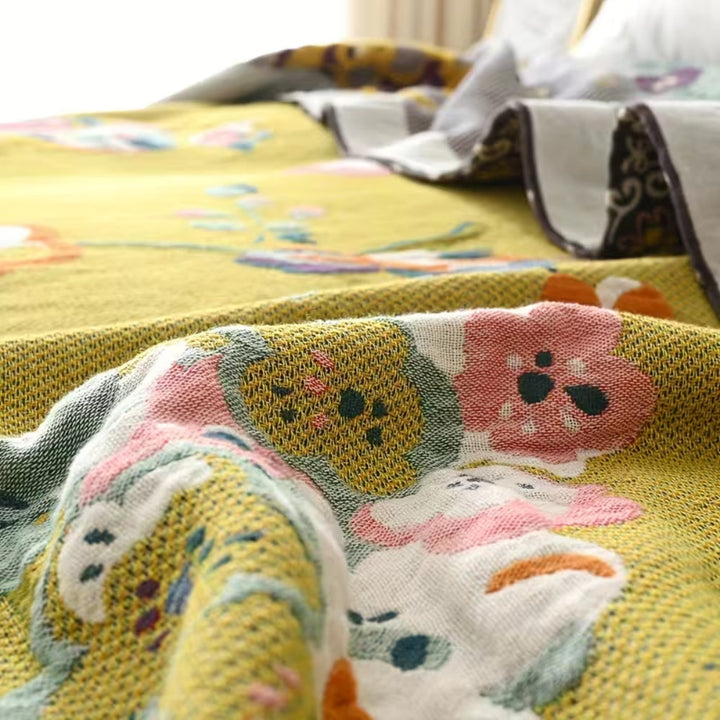 Close-up of a yellow cotton blanket with a colorful floral and bird pattern, featuring pink, white, and green flowers.