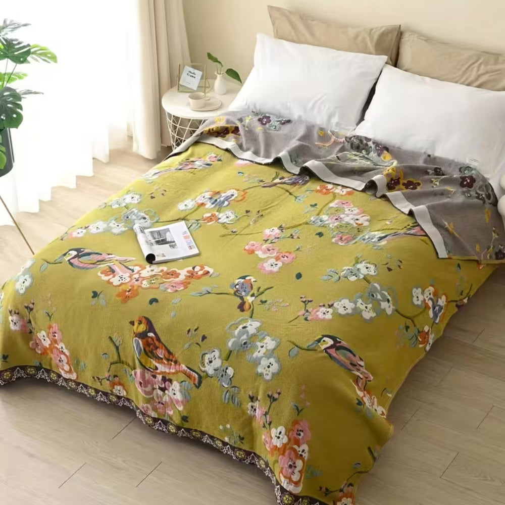 Boho garden bird floral blanket in olive green with birds and flowers, folded on a bed with pillows.
