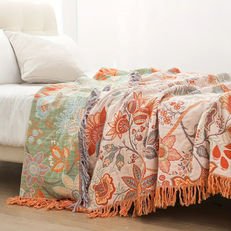 Cotton floral throw blanket with fringe trim in green and cream with orange and blue floral patterns.