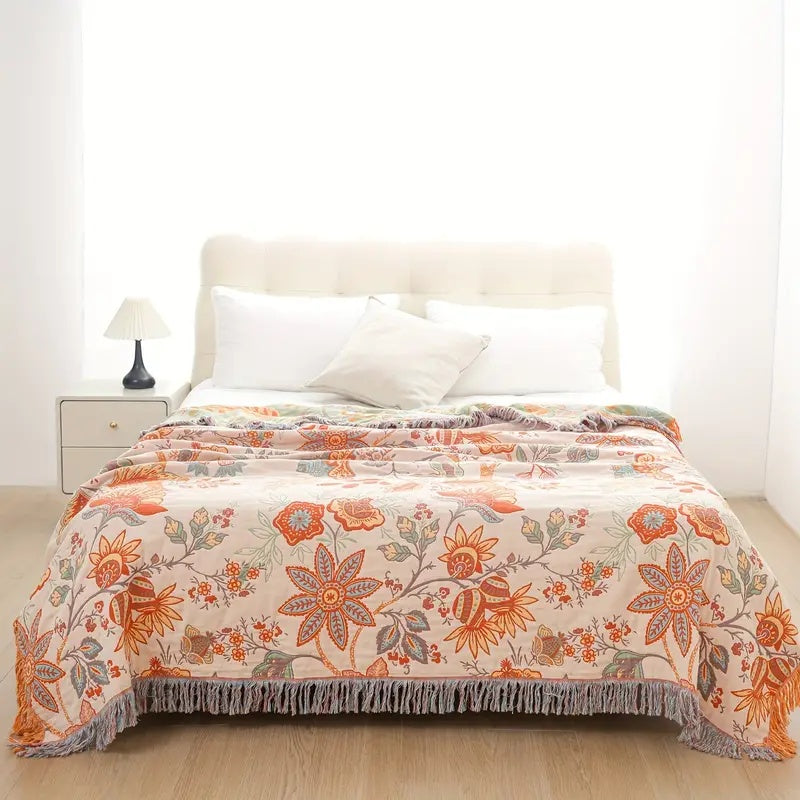 Cream cotton throw blanket with a floral pattern in orange and blue, featuring fringe trim.