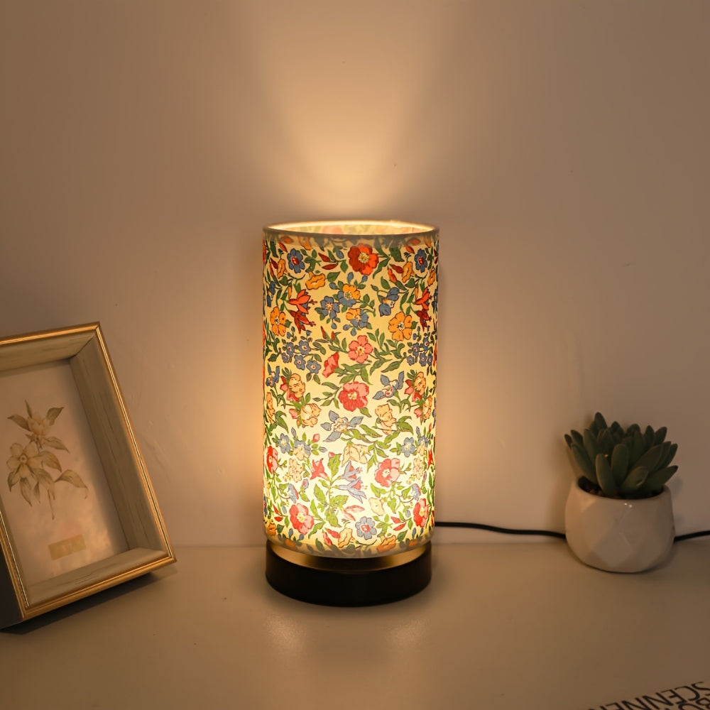 Botanical floral fabric table lamp with a warm ambient glow, next to a framed picture and a potted succulent.