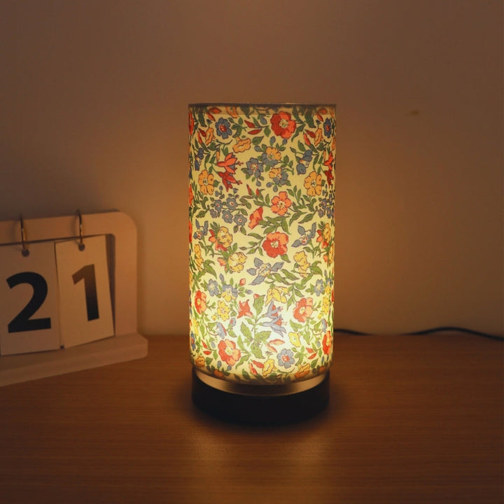 Botanical floral fabric table lamp with a warm ambient glow, next to a desk calendar showing the 21st.