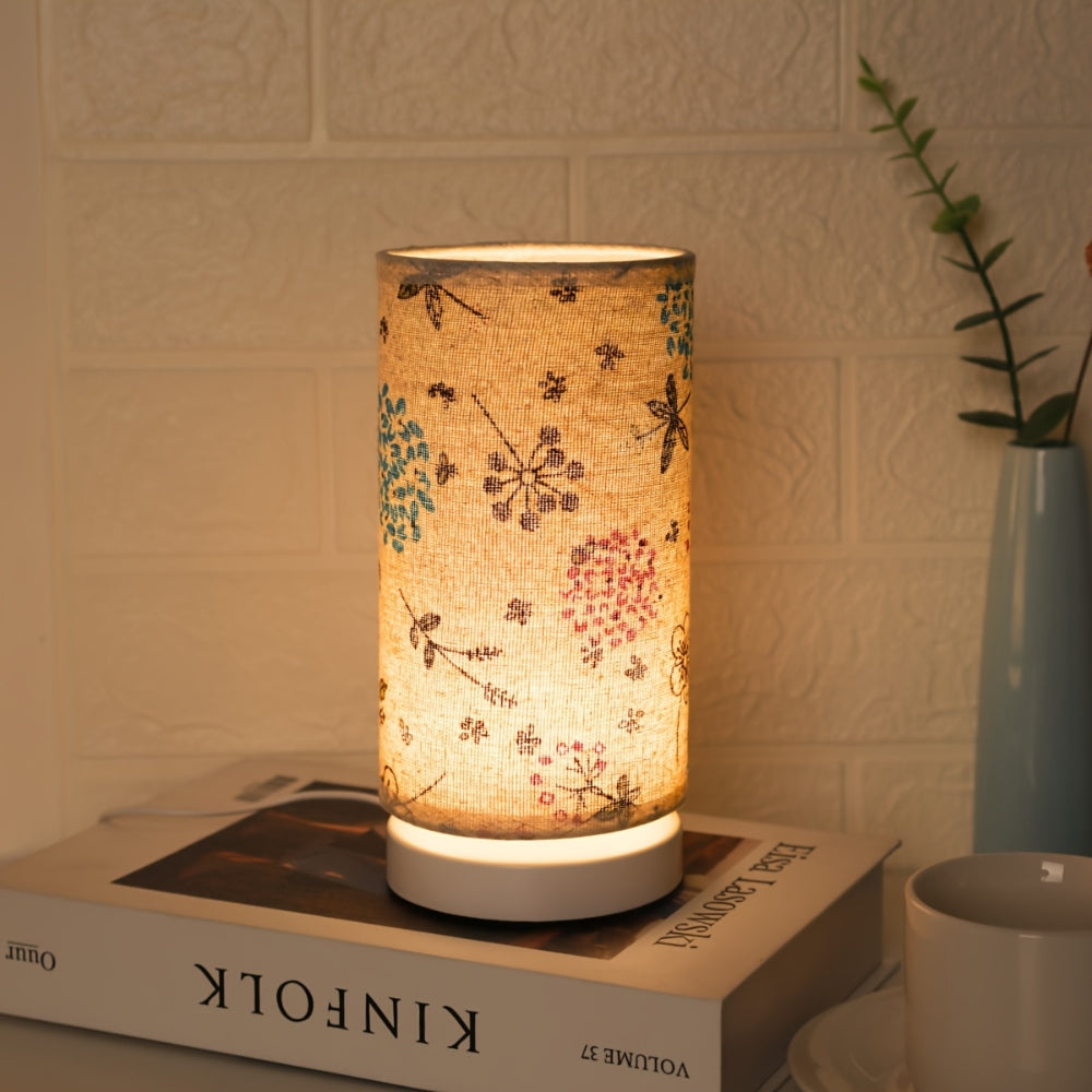 Botanical floral fabric table lamp with a warm ambient glow on a stack of books.