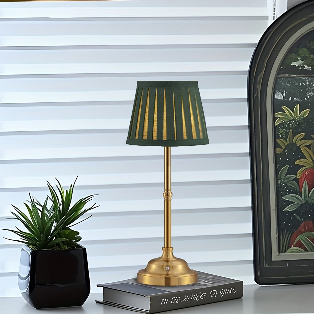Brass finish cordless table lamp with a dark green pleated shade sits on a book.
