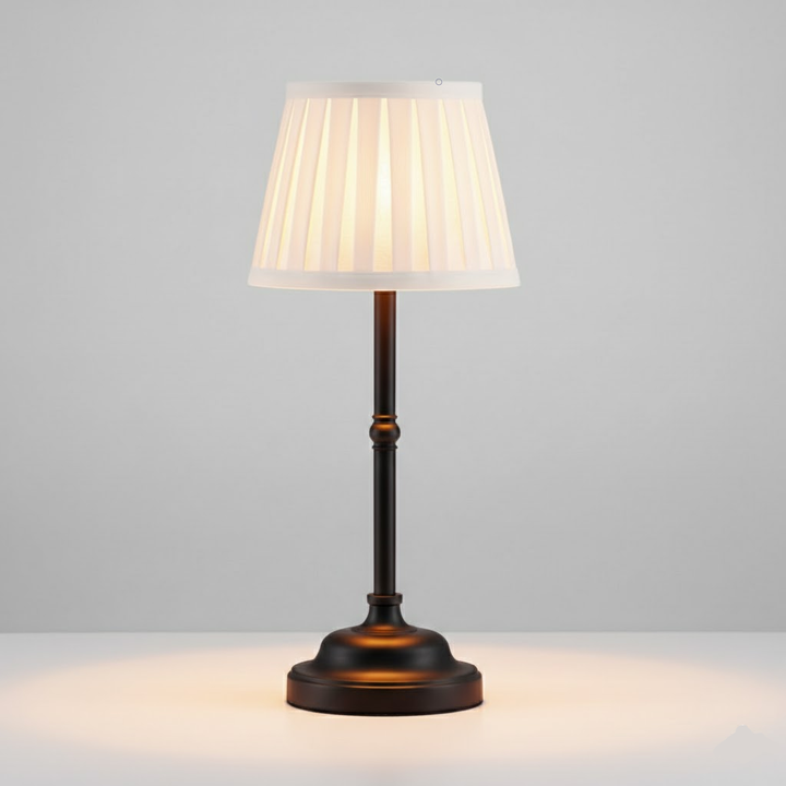 A dark metal cordless table lamp with a pleated white shade, illuminated from within.