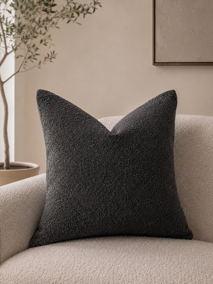 Dark grey textured pillow cover on a cream boucle armchair.