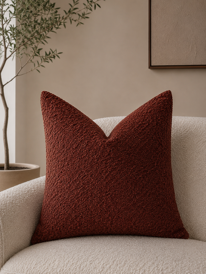 Calen Soft Pillow Cover in a textured rust color on a cream boucle chair.