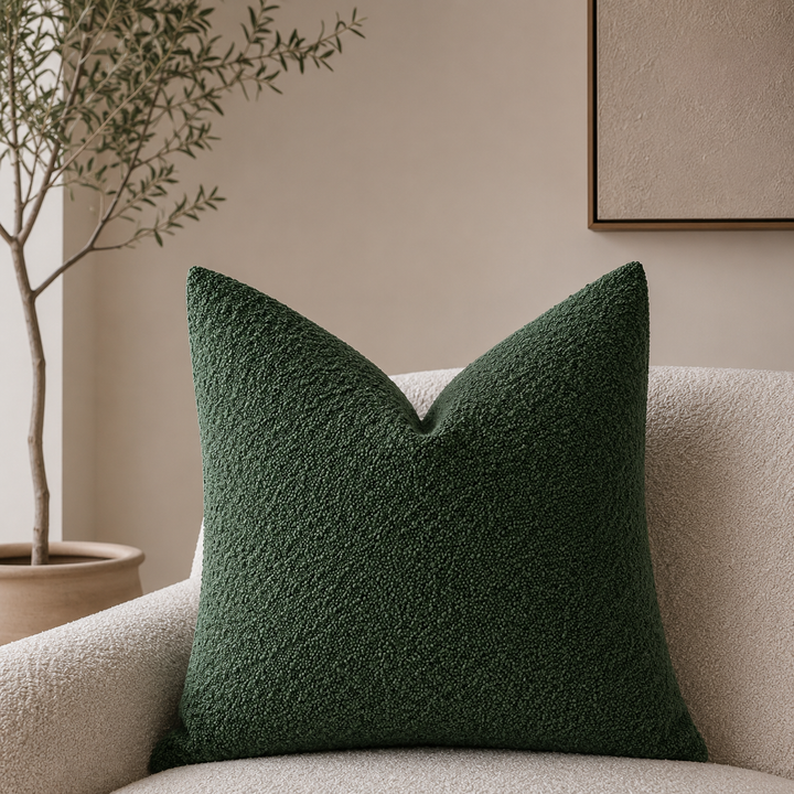 Dark green textured pillow cover on a cream boucle armchair.