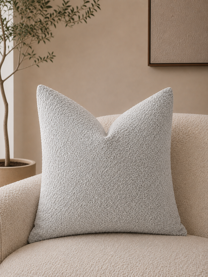 Light grey textured Calen pillow cover on a cream boucle armchair.