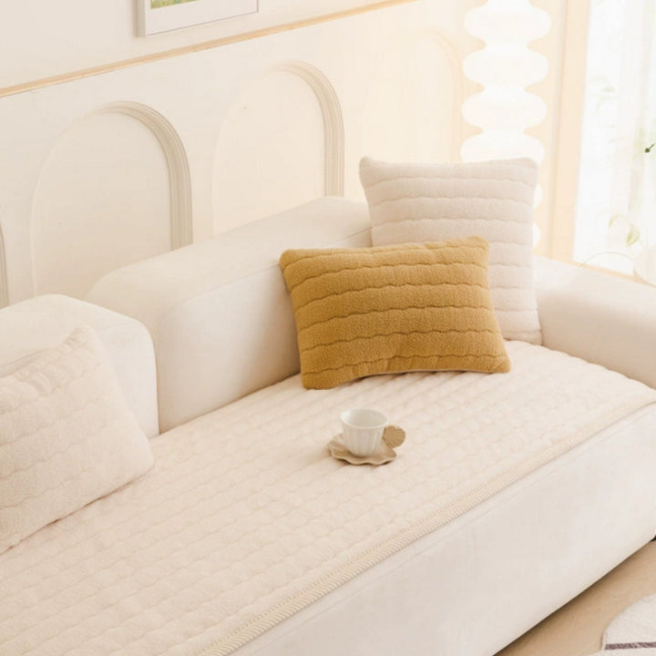 Cream-colored plush sofa cover with textured pillows and a teacup.