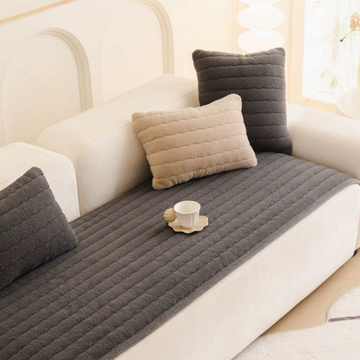 Thick plush sofa cover in dark gray with beige and dark gray pillows and a white teacup.