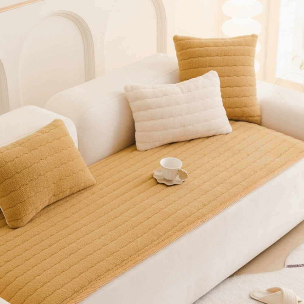 A plush sofa cover in a warm yellow hue with textured stripes, featuring decorative pillows and a teacup.