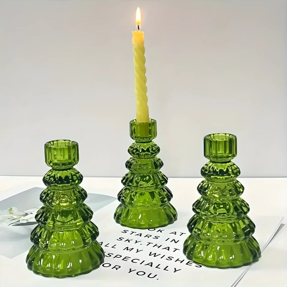 Three green glass Christmas tree-shaped candle holders, one with a lit yellow candle.