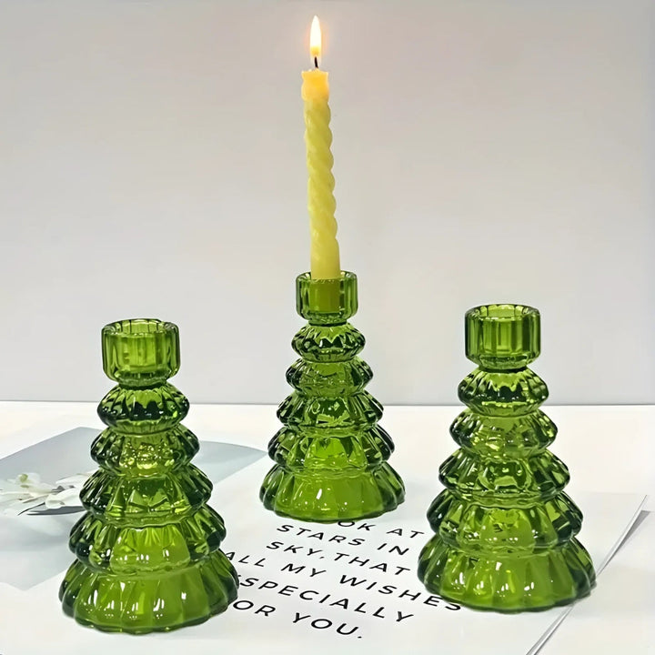 Three green glass Christmas tree-shaped candle holders, one with a lit yellow candle.