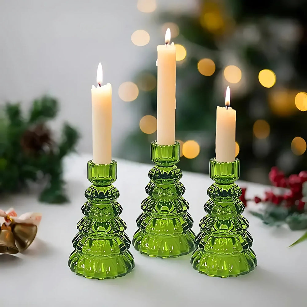 Three green glass Christmas tree-shaped candle holders with lit white candles.