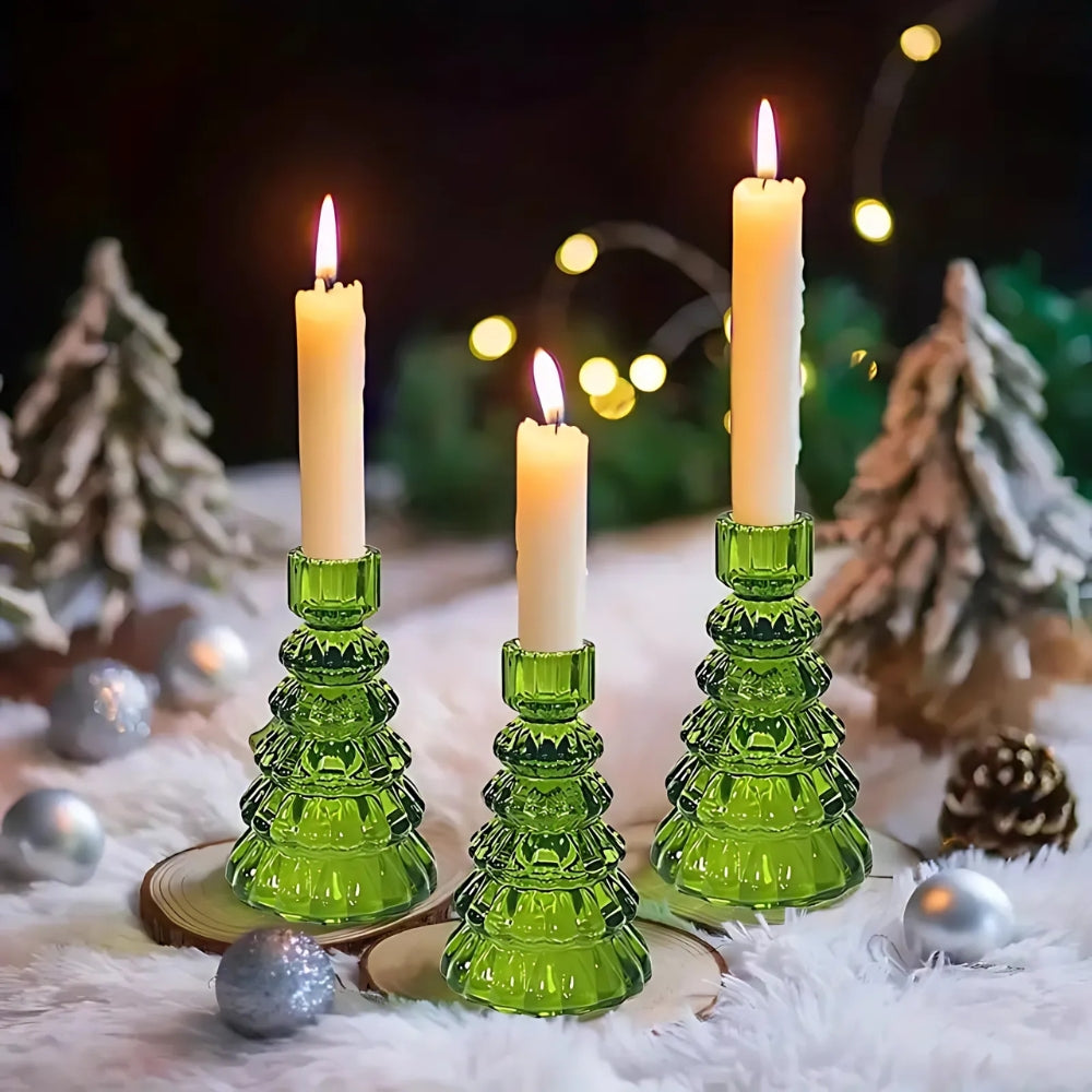 Three green glass Christmas tree candle holders with lit white taper candles.