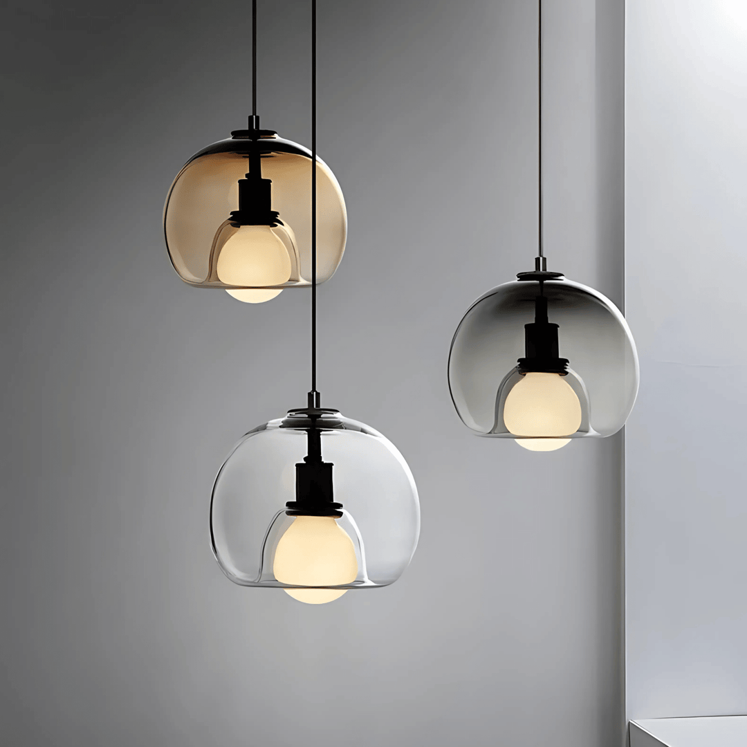 Three handblown glass pendant lights with amber and clear shades hanging against a grey wall.