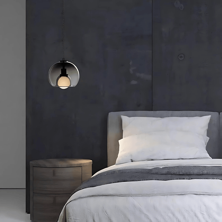 Handblown glass pendant light with a clear spherical shade and a visible bulb, hanging above a bedside table.