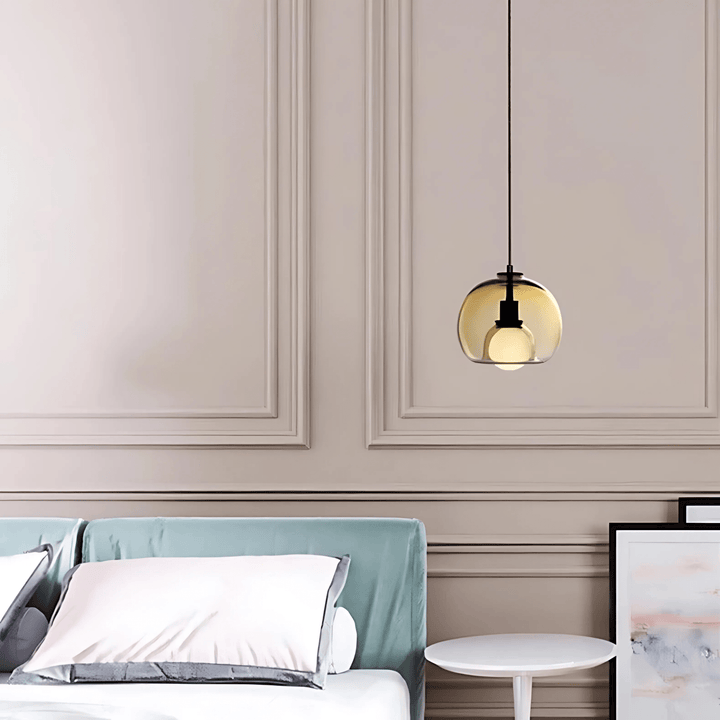 Amber handblown glass pendant light with a black cord hanging over a bed.